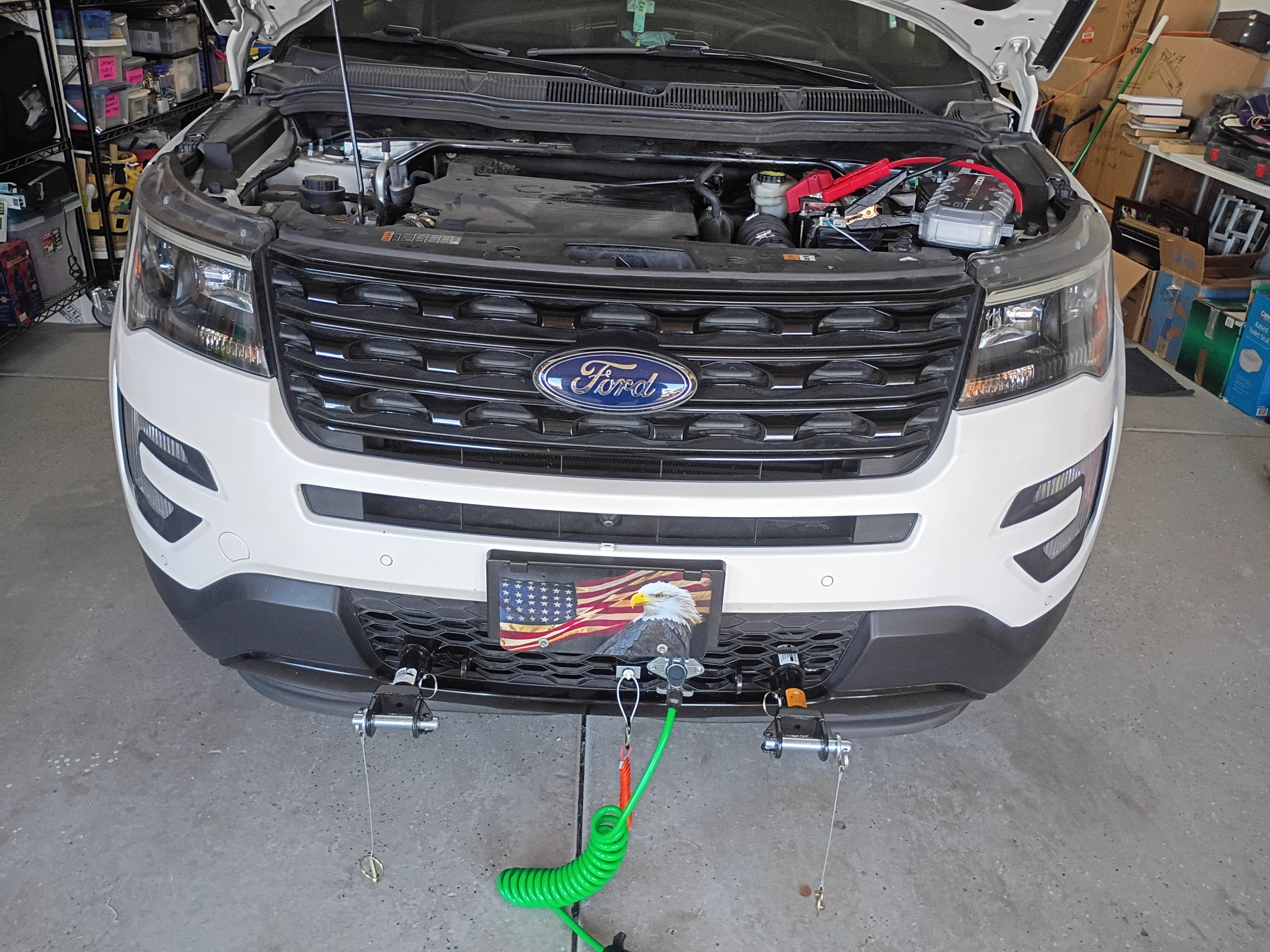 A man adjusts a trailer hook with wheels, orange and yellow electronics on its bed, a parking lot and trees in the backgro...
